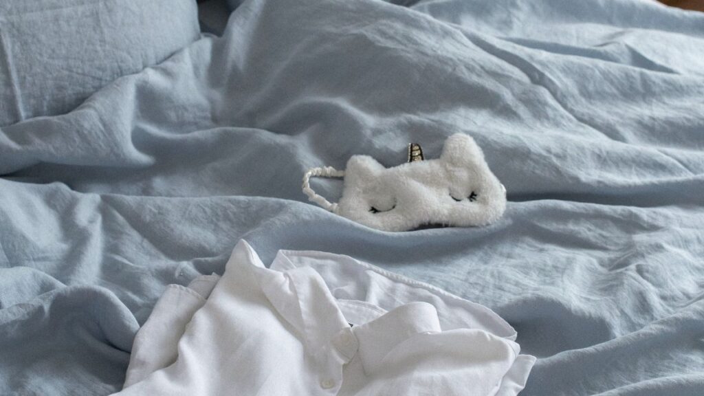 Unmade bed with folded pajamas and sleeping mask on top